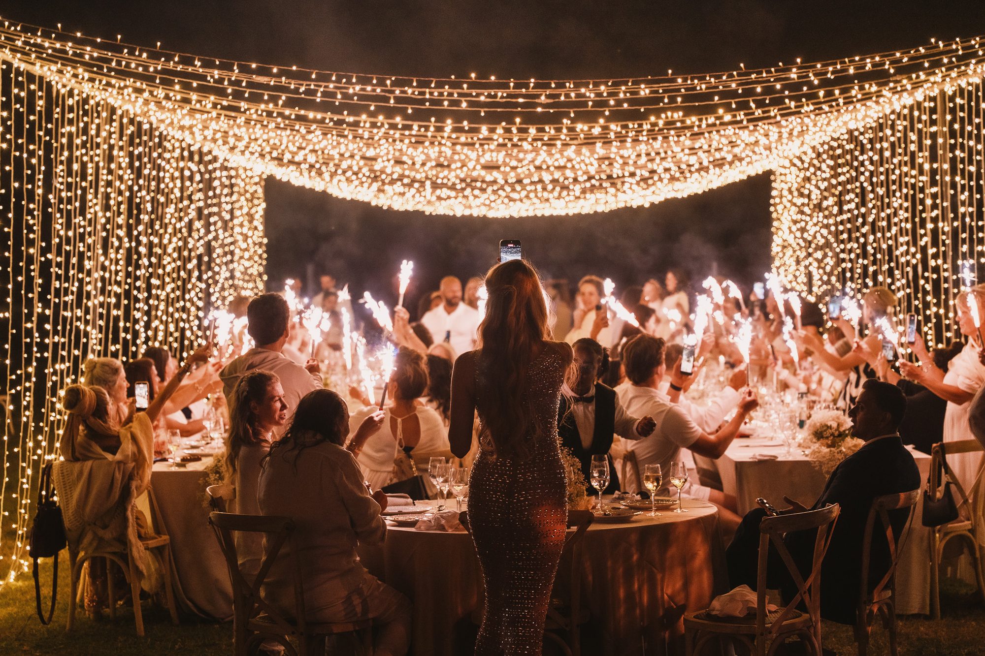 A LumiVitae gathering under a canopy of fairy lights, guests raising sparklers