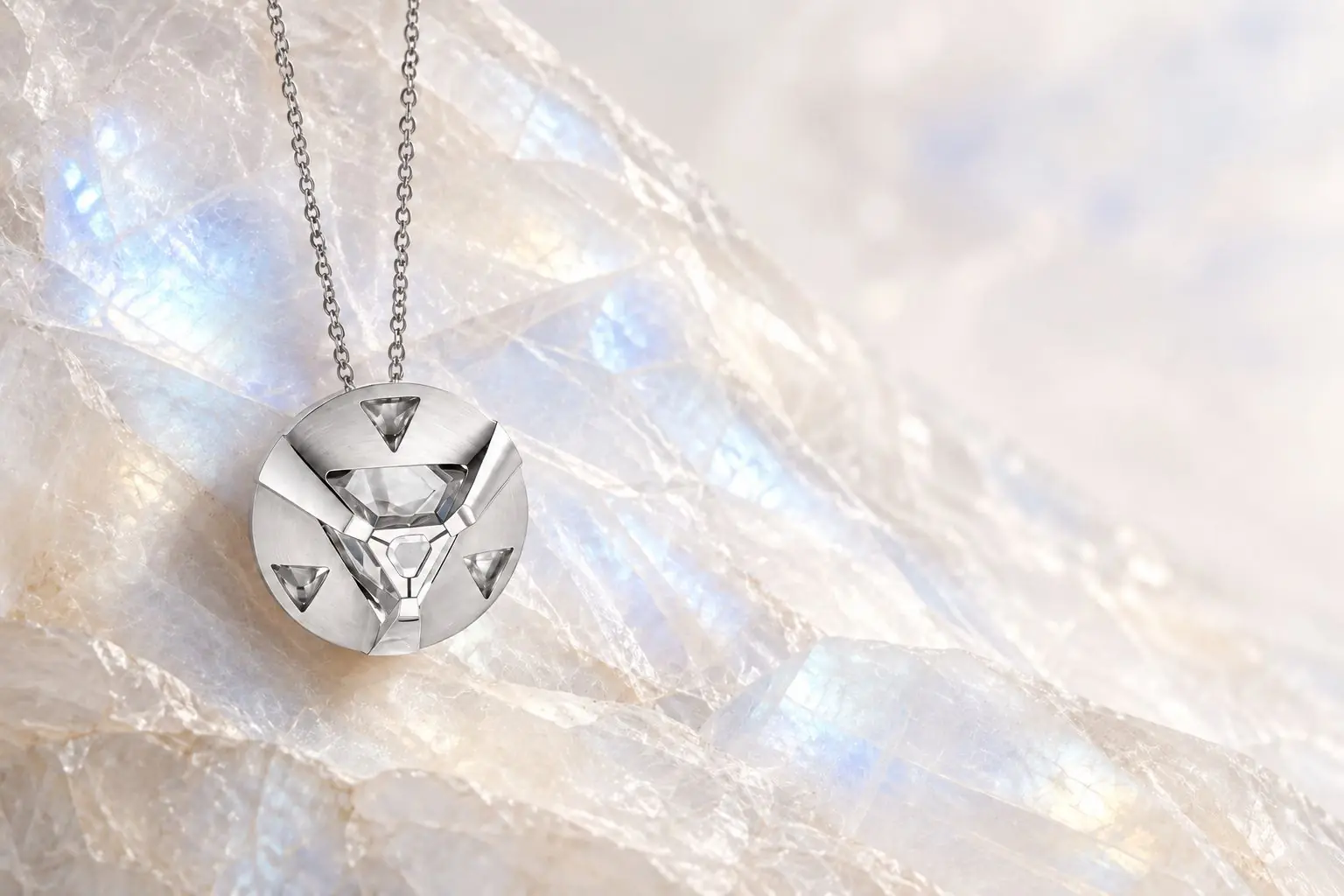 A silver ARQ pendant resting on luminous moonstone